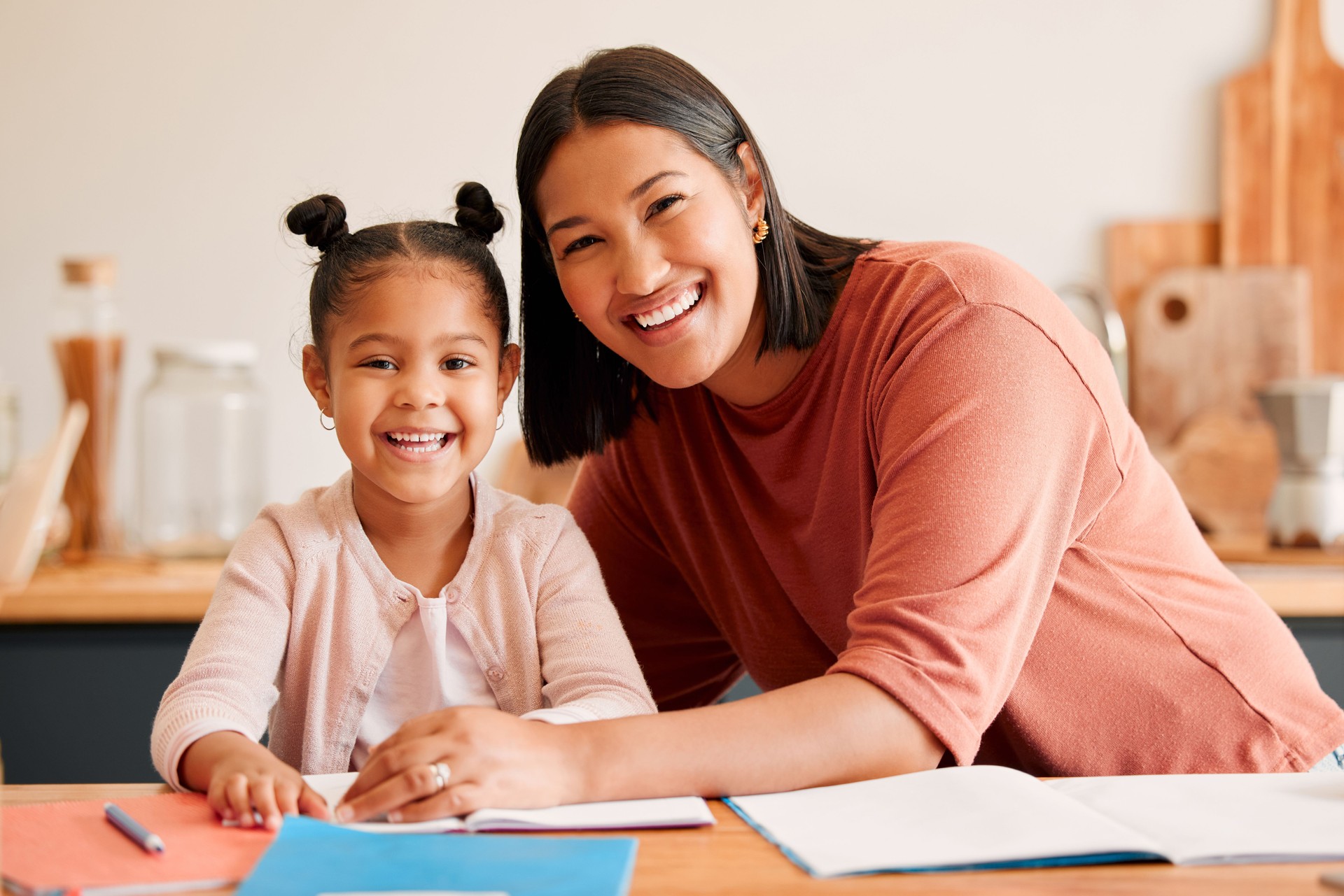 Mother helping, teaching and educating daughter with homework at home. Portrait of happy, loving and smiling mom and little girl busy with educational lesson, tutoring or assistance at home together
